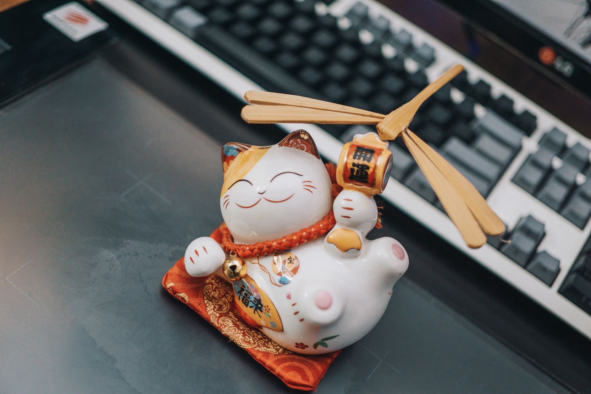A ceramic Maneki Neko figurine sitting on a desk beside a keyboard, symbolizing luck and prosperity.
