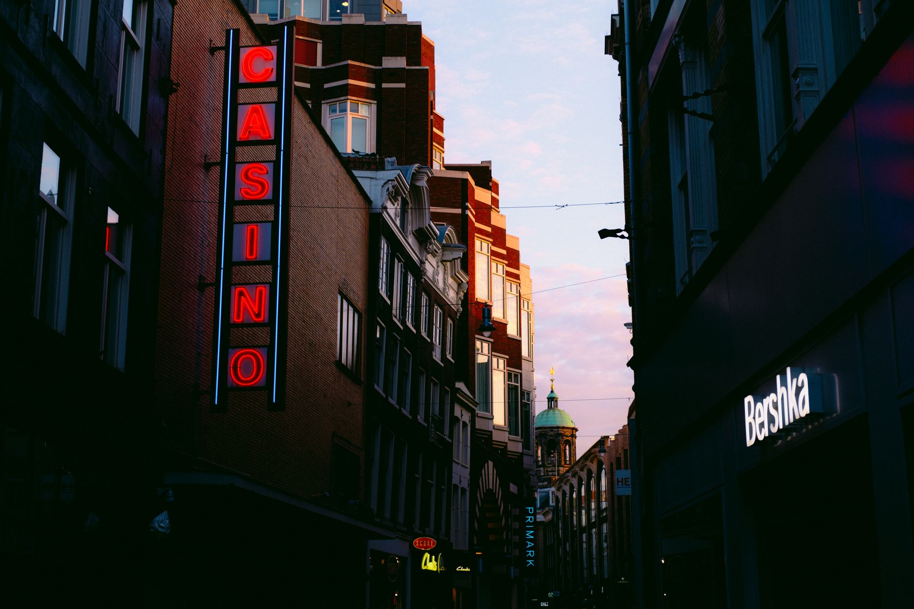 Urban cityscape at dusk featuring neon signs and illuminated streets, creating a lively atmosphere.