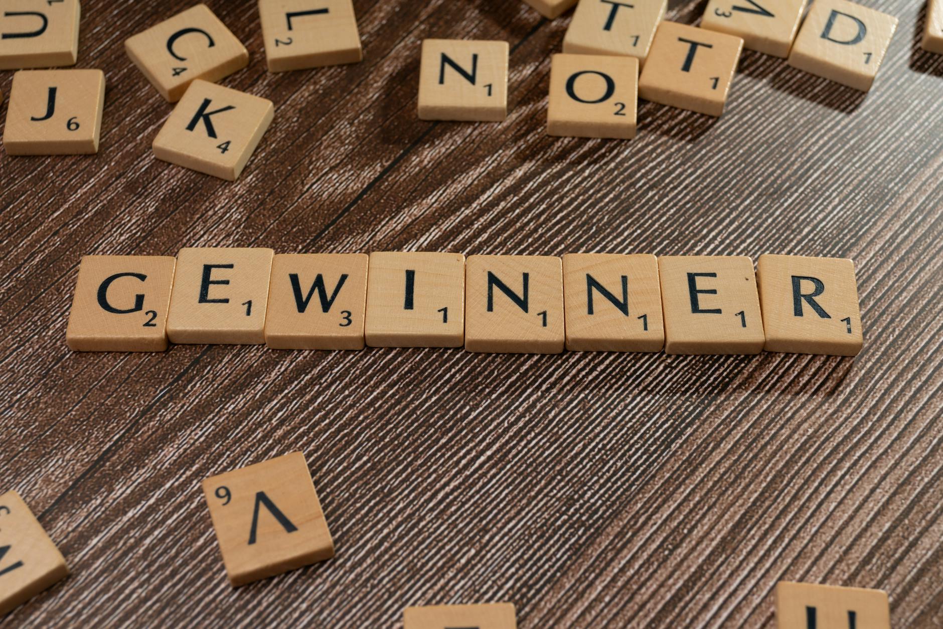 Scrabble tiles forming the word 'Gewinner' meaning winner on a wooden table.