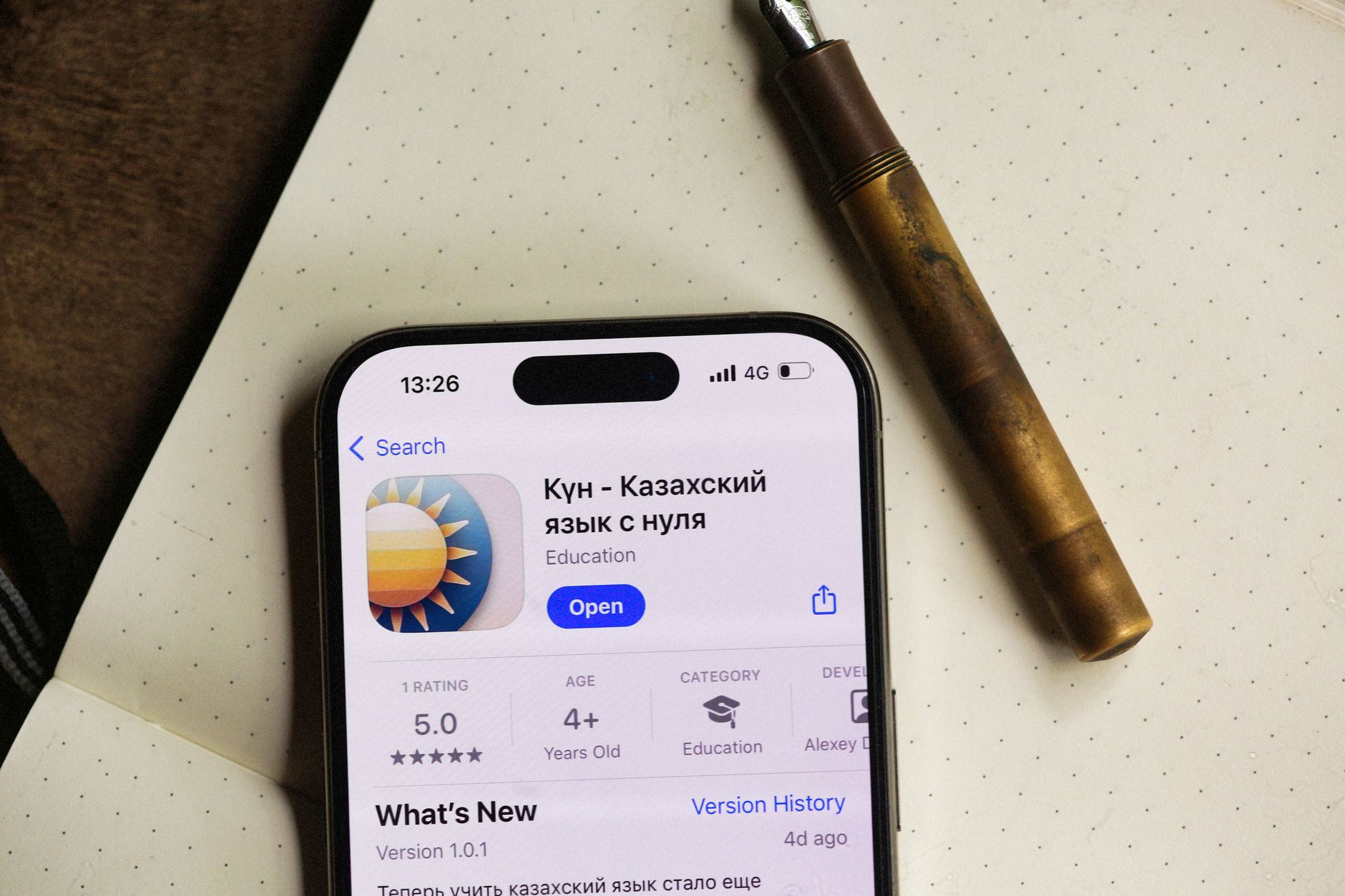 Smartphone screen shows an educational app interface with a pen nearby on dotted paper.