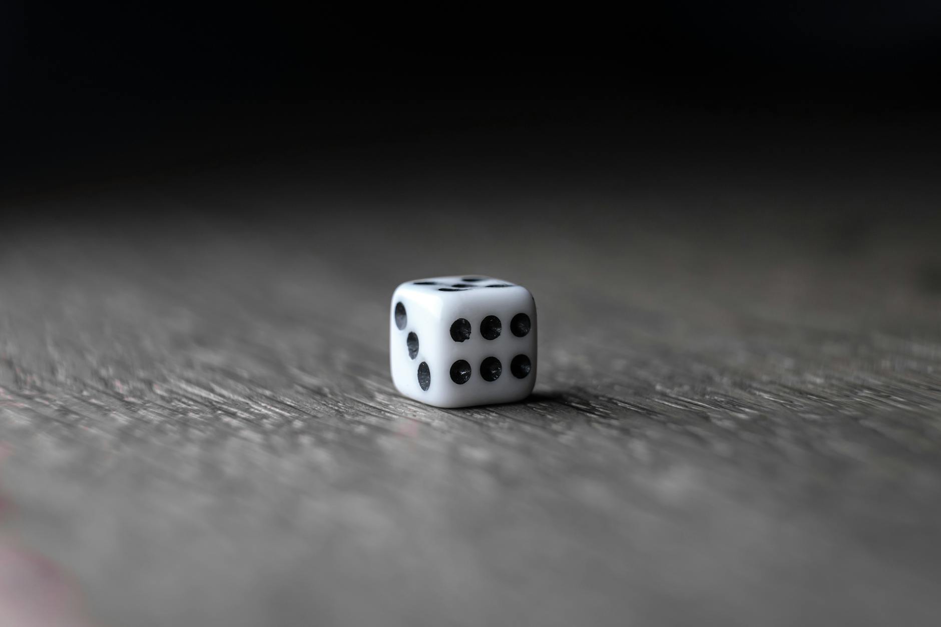 Closeup of white small plastic dice for boardgame placed on wooden desk against dark background