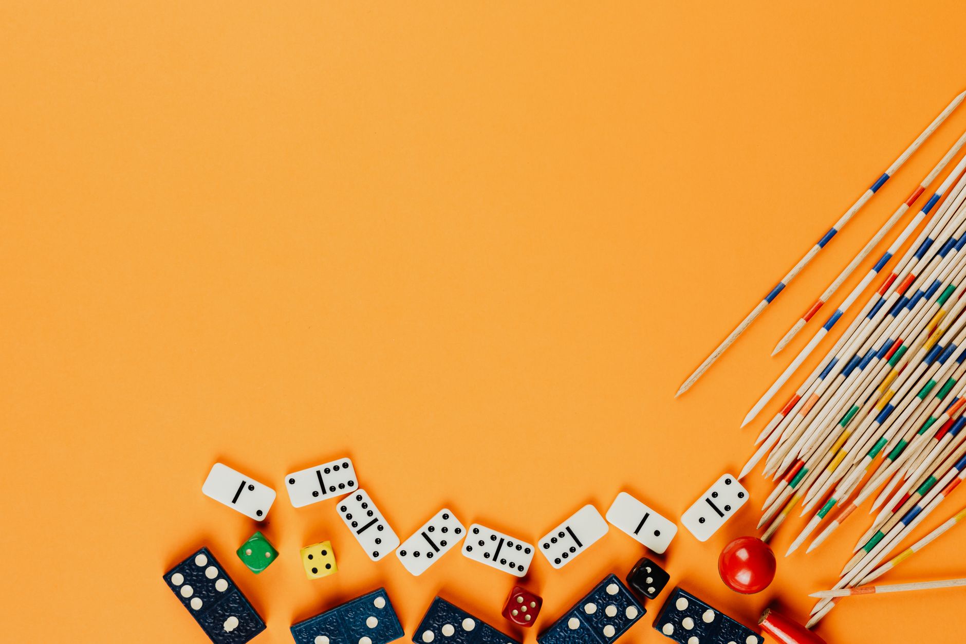 Top view of dominoes, dices, and colorful game sticks scattered on an orange background.