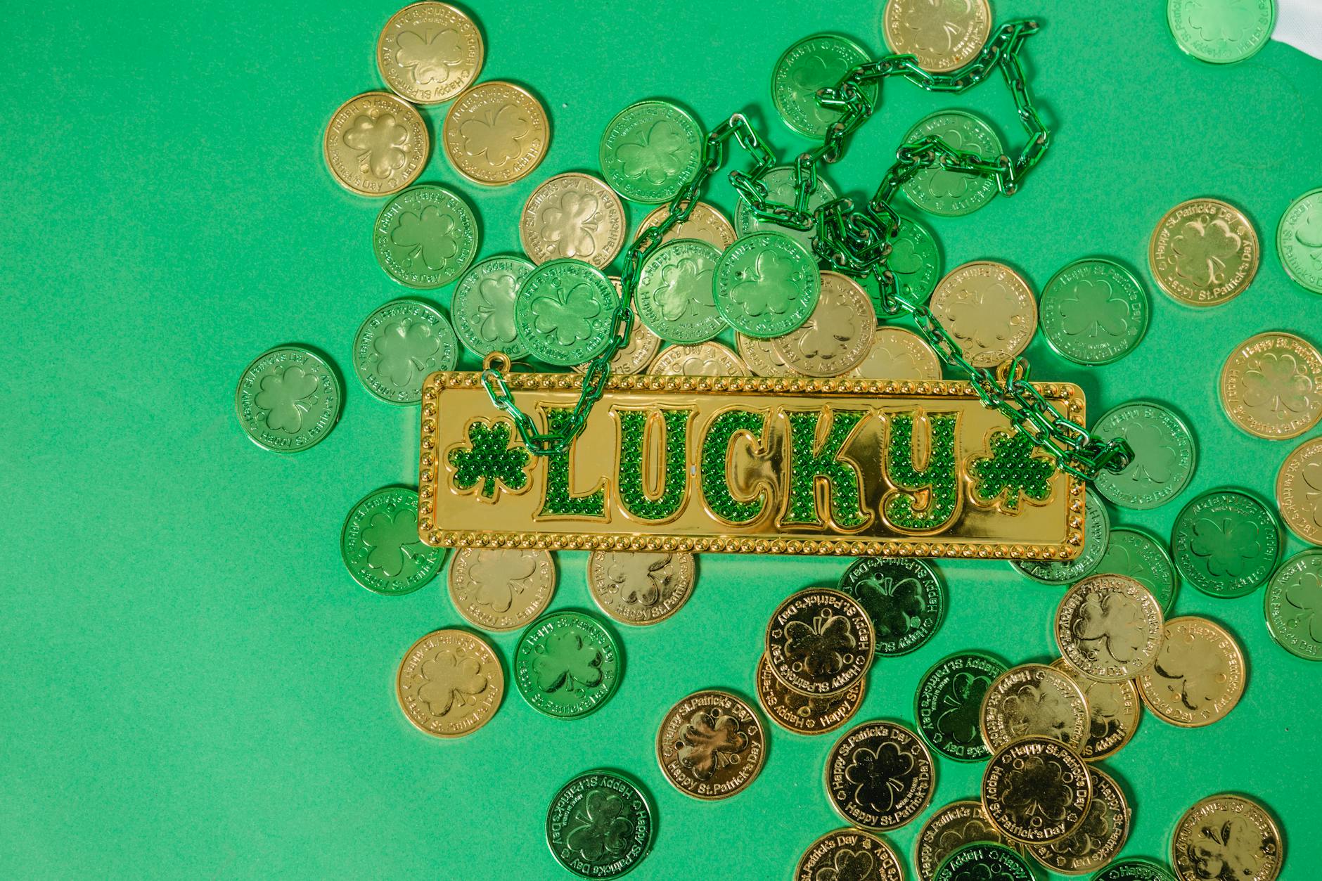 From above of golden lucky charm with green chain on heap of shiny coins on green surface