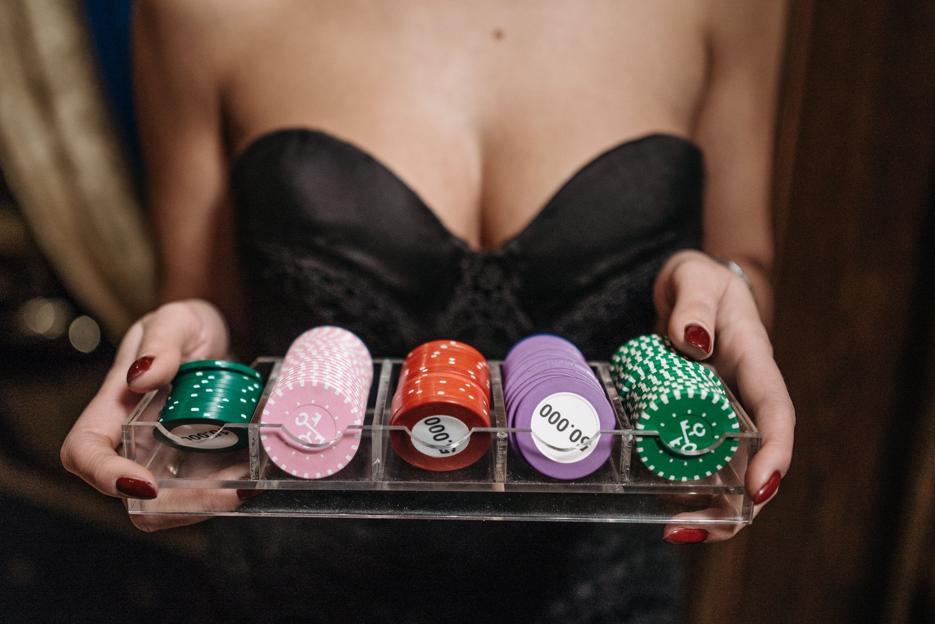 A person holding a tray of colorful casino chips, dressed in elegant evening wear, showcasing gambling themes.