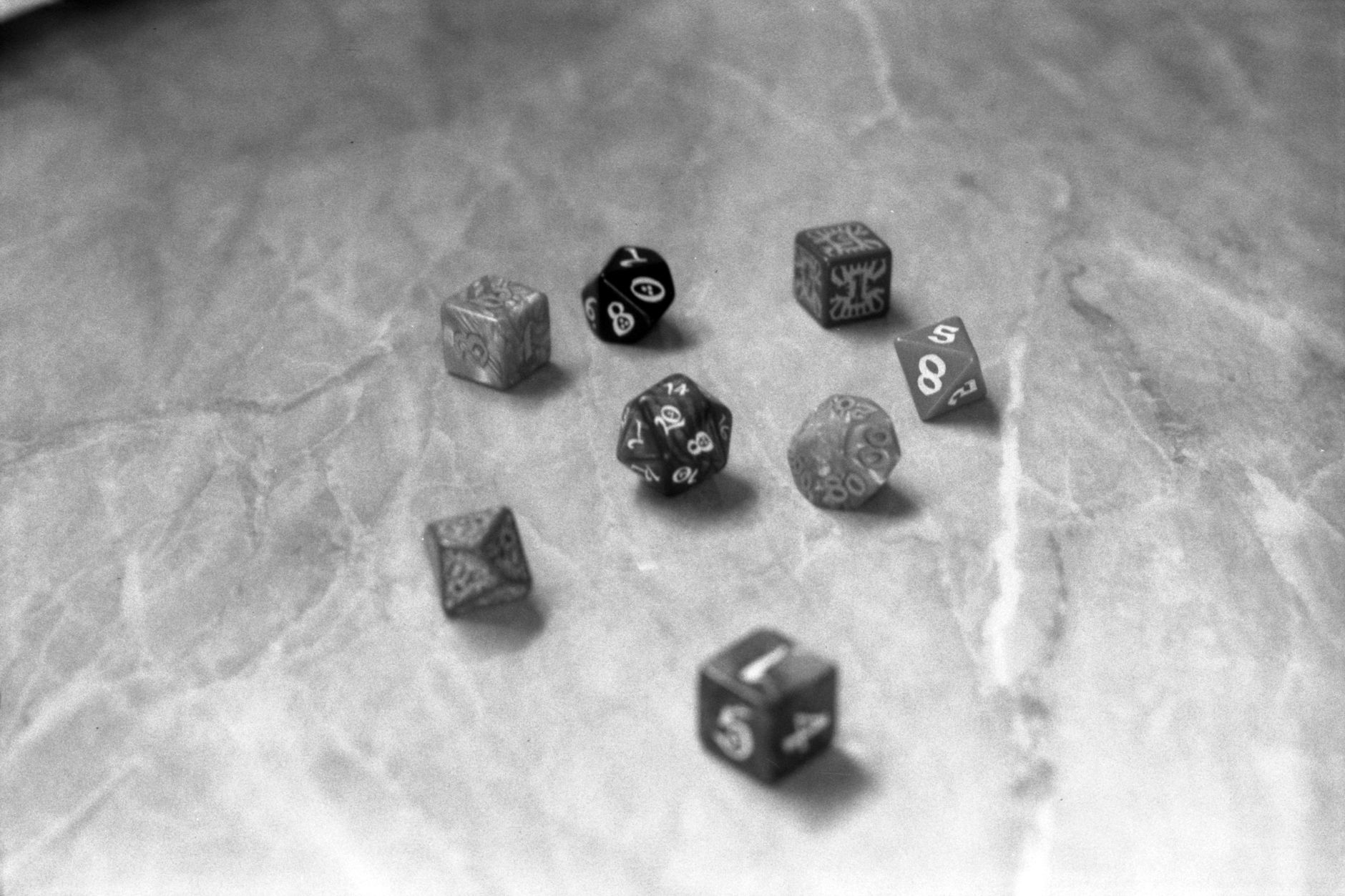 Black and white image of role-playing dice on a marble surface, highlighting gaming and strategy.