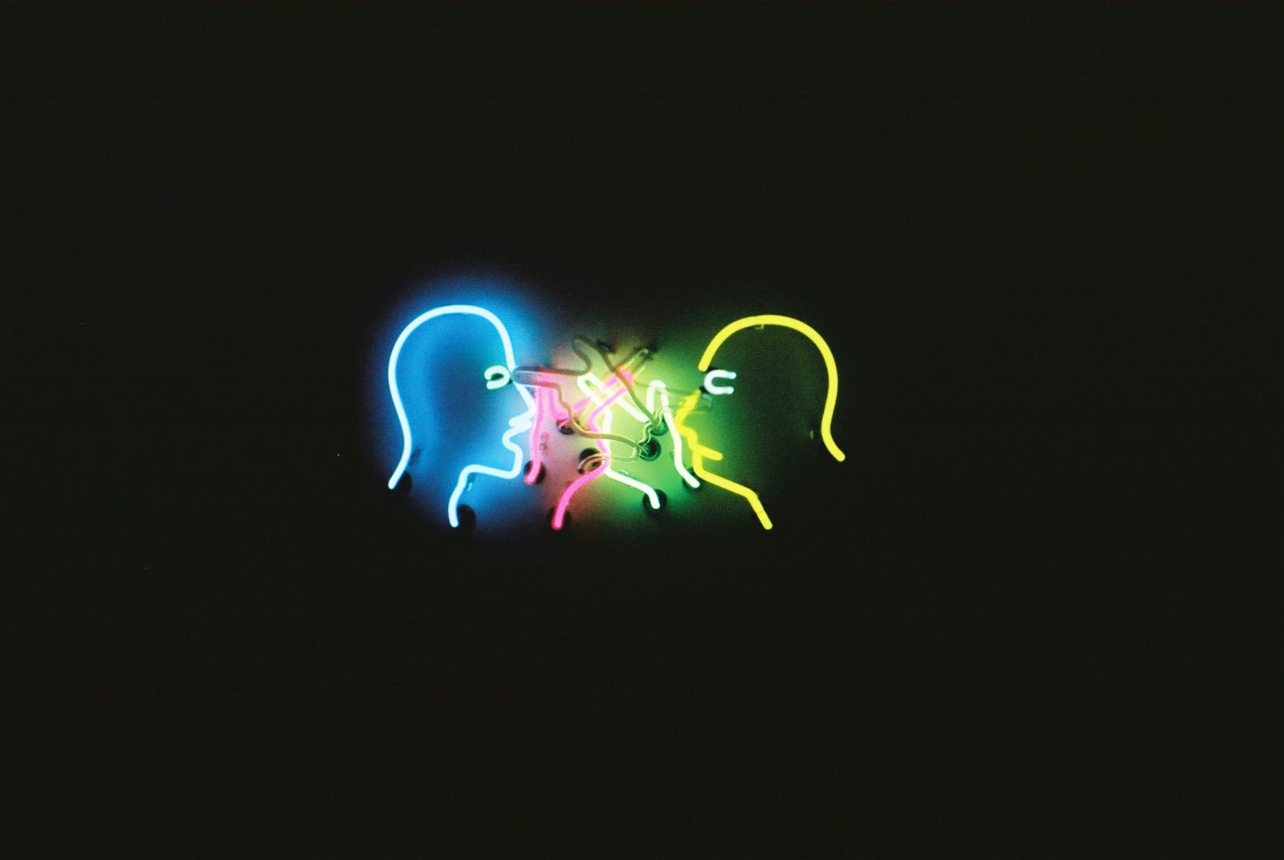 Colorful neon light art installation depicting faces on a dark background.